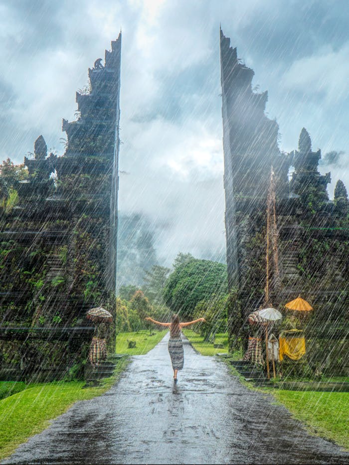 services-01 Woman in vibrant rain at iconic Handara Gate, Bali. A magical travel moment.