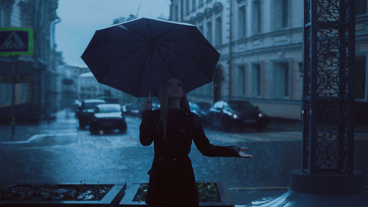 services-03 Woman under an umbrella during a rainy day in a moody cityscape scene.